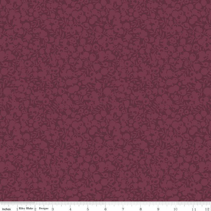 A close-up of a repeating floral pattern in deep burgundy and muted mauve, with a ruler strip along the bottom showing scale.
