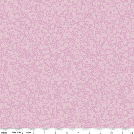A close-up of a light violet fabric with a repeating small floral and leaf pattern in a slightly darker violet. A ruler along the bottom edge shows measurements in inches and includes the text 'Riley Blake Designs'.