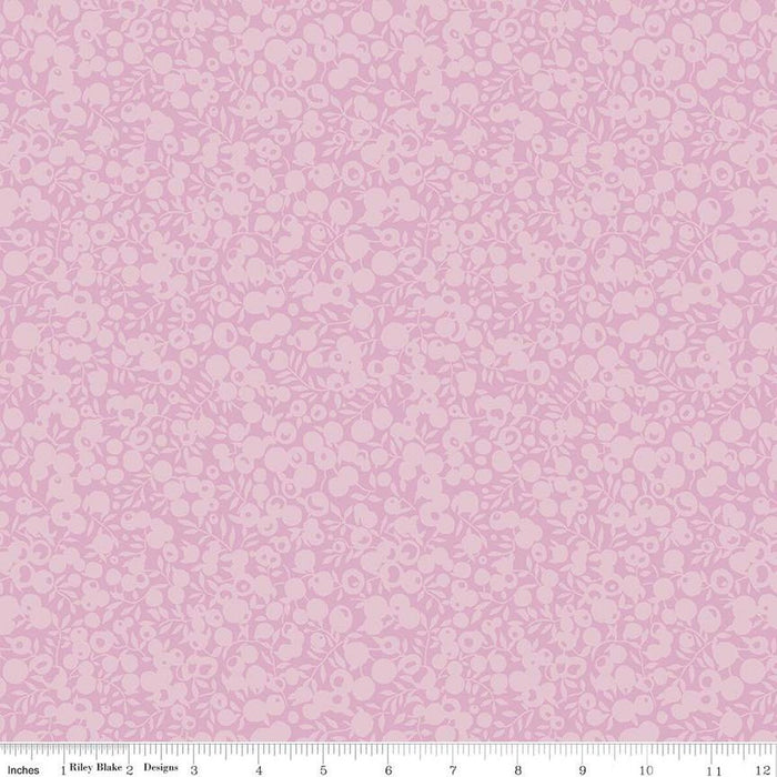 A close-up of a light violet fabric with a repeating small floral and leaf pattern in a slightly darker violet. A ruler along the bottom edge shows measurements in inches and includes the text 'Riley Blake Designs'.