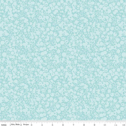 A close-up of a fabric pattern featuring a light aqua background with a dense, repeating white floral and leaf motif. A white ruler along the bottom edge displays the brand 'Riley Blake Designs' and shows the pattern repeats in scale.