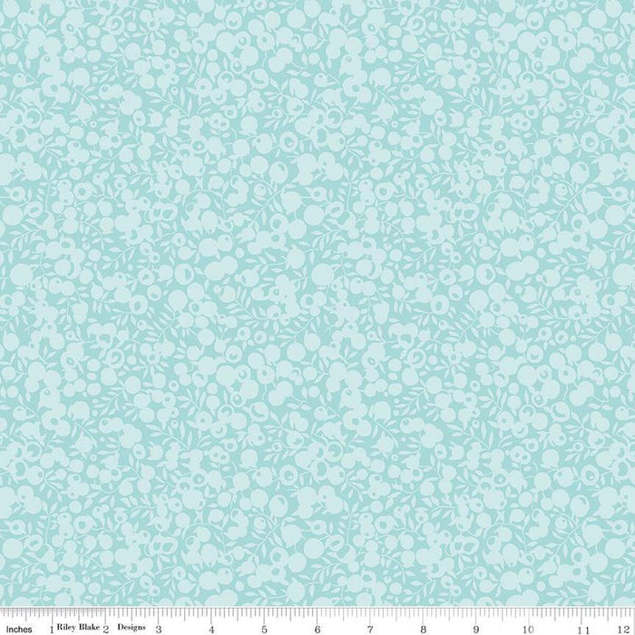 A close-up of a fabric pattern featuring a light aqua background with a dense, repeating white floral and leaf motif. A white ruler along the bottom edge displays the brand 'Riley Blake Designs' and shows the pattern repeats in scale.