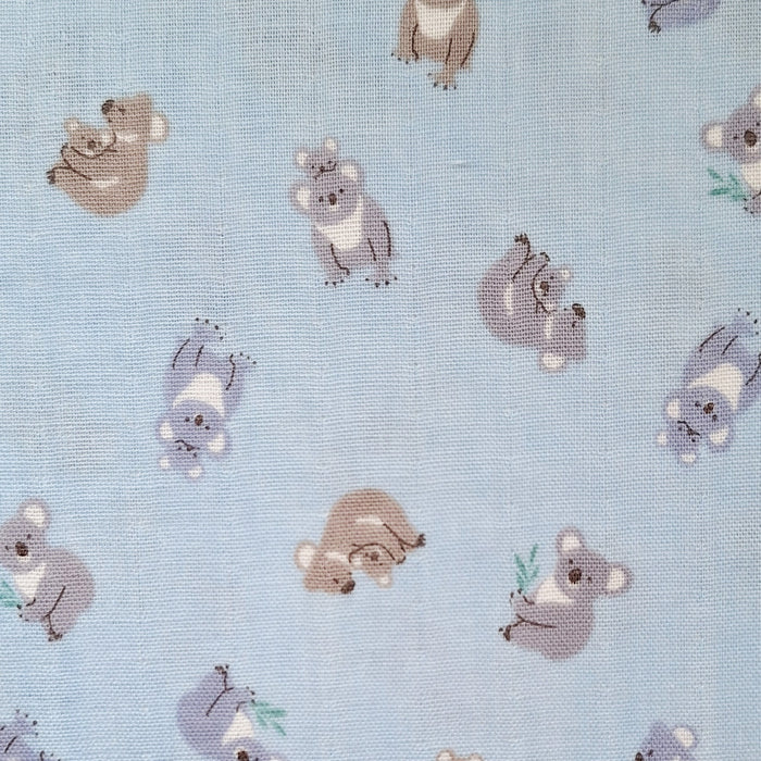 Light blue fabric with a repeating pattern of cute cartoon koalas in muted gray, brown, and white tones.