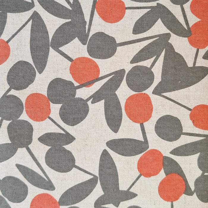 A close-up of a fabric or wallpaper pattern featuring stylized dark gray cherries with orange-red fruit on an off-white textured background.