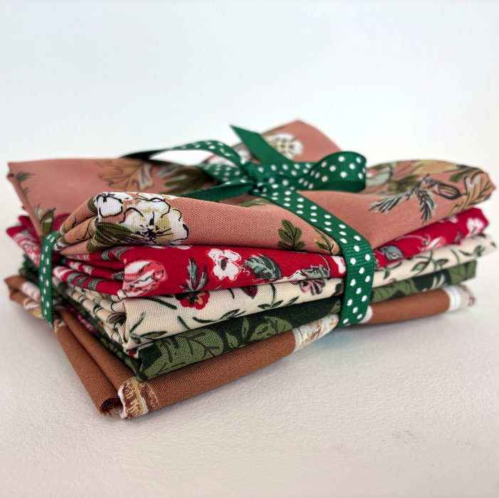 Stack of folded fabric with floral patterns tied with a green ribbon on a white background