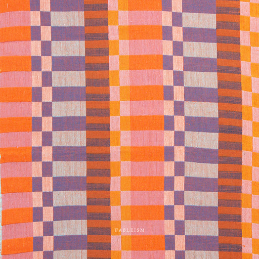 close up shot of yarn dyed fabric in pink orange and purple with varying size checks