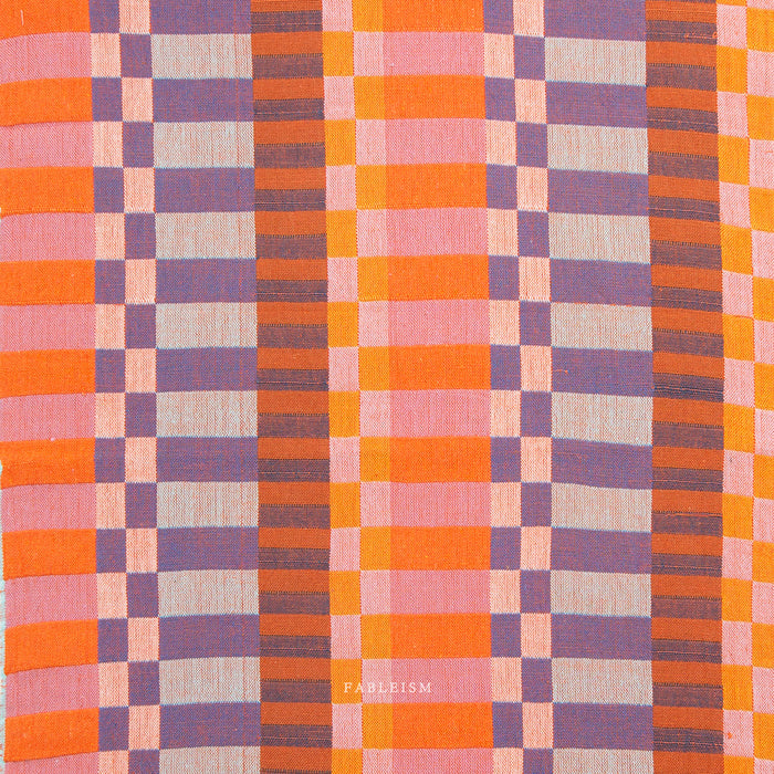 close up shot of yarn dyed fabric in pink orange and purple with varying size checks