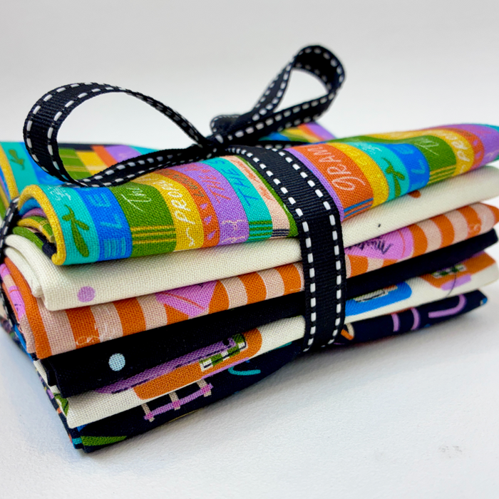 A bundle of folded patterned fabric pieces tied together with a black ribbon featuring white polka dots, photographed on a clean white background.