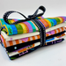 A bundle of folded patterned fabric pieces tied together with a black ribbon featuring white polka dots, photographed on a clean white background.