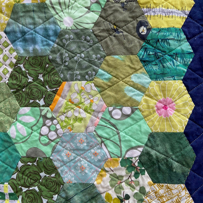 Hexagonal patchwork quilt with a variety of green patterns on a blue background