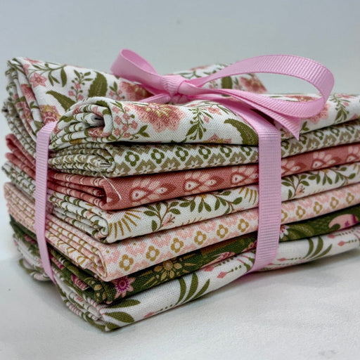 A stack of folded patterned fabric pieces tied together with a pink ribbon bow, photographed on a plain light background.
