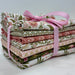 A stack of folded patterned fabric pieces tied together with a pink ribbon bow, photographed on a plain light background.