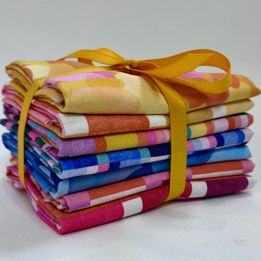 A stack of colorful patterned fabric squares tied together with a yellow ribbon, photographed on a plain light background.
