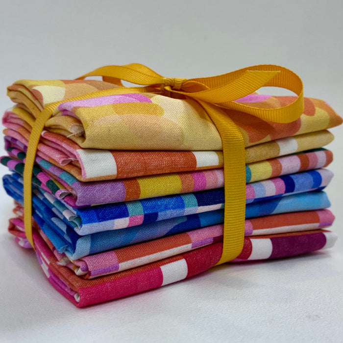 A stack of colorful patterned fabric squares tied together with a yellow ribbon, photographed on a plain light background.