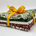 A stack of folded patterned fabric pieces tied with a bright yellow ribbon, photographed on a clean white background.