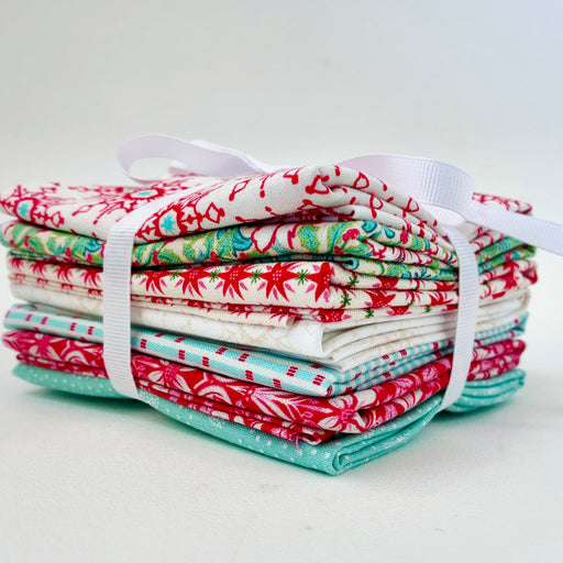 close up of fabric bundle with small pieces of fabric folded and wrapped with  a white ribbon, the fabric is a mix of patterns in red, white and teal.