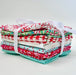 close up of fabric bundle with small pieces of fabric folded and wrapped with  a white ribbon, the fabric is a mix of patterns in red, white and teal.
