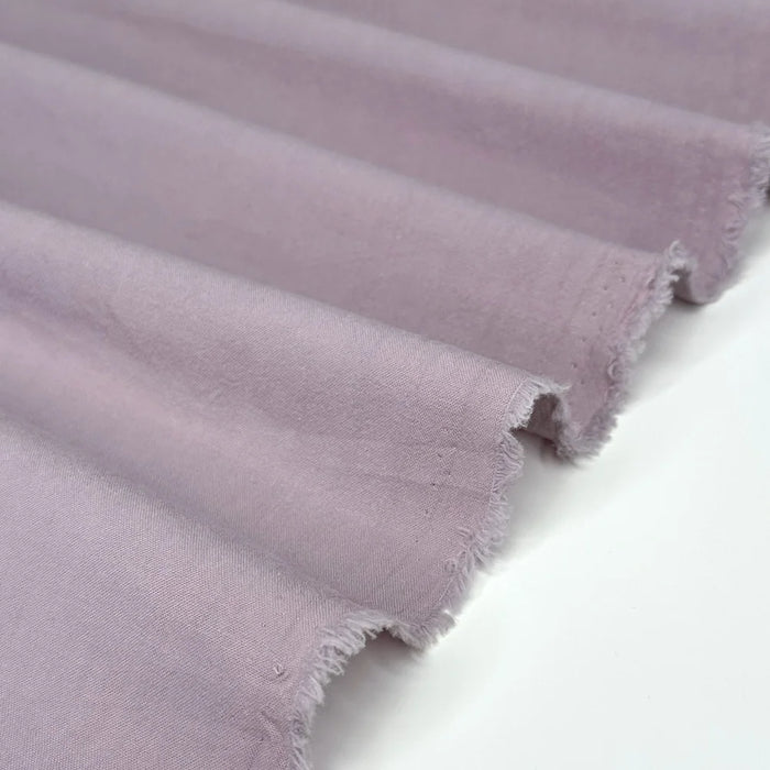 A close-up of draped dusty purple fabric with a frayed, raw edge, shown against a plain white background.