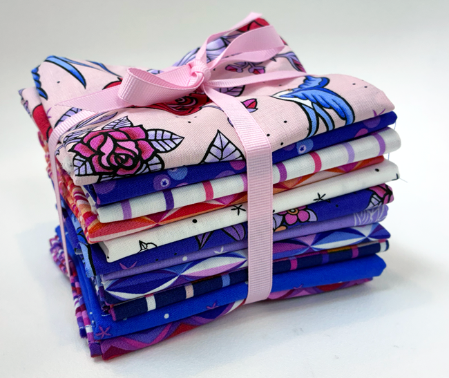 Stack of colorful fabric bundles tied with a pink ribbon on a white background