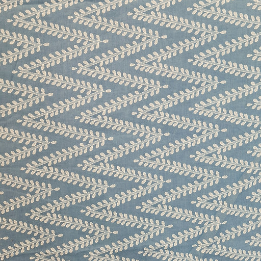A close-up of a fabric pattern featuring a repeating chevron design of cream-colored leafy branches on a dusty slate blue background.