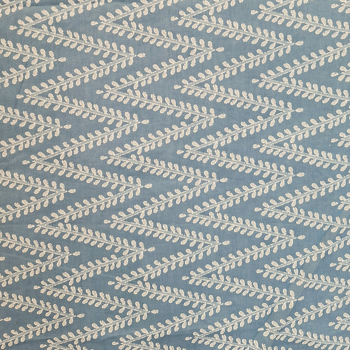 A close-up of a fabric pattern featuring a repeating chevron design of cream-colored leafy branches on a dusty slate blue background.