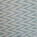 A close-up of a fabric pattern featuring a repeating chevron design of cream-colored leafy branches on a dusty slate blue background.