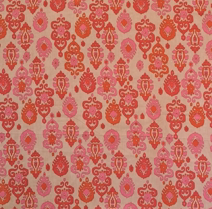 A close-up of a woven fabric with an all-over repeating damask pattern in shades of pink, coral, and orange on a warm beige background.