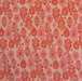 A close-up of a woven fabric with an all-over repeating damask pattern in shades of pink, coral, and orange on a warm beige background.