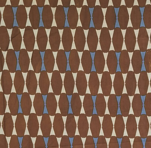A close-up of a patterned fabric or wallpaper featuring a repeating geometric design of brown elongated ovals, cream triangles, and small light blue diamond accents.