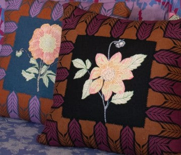 Two embroidered pillows with floral designs on a patterned fabric background.