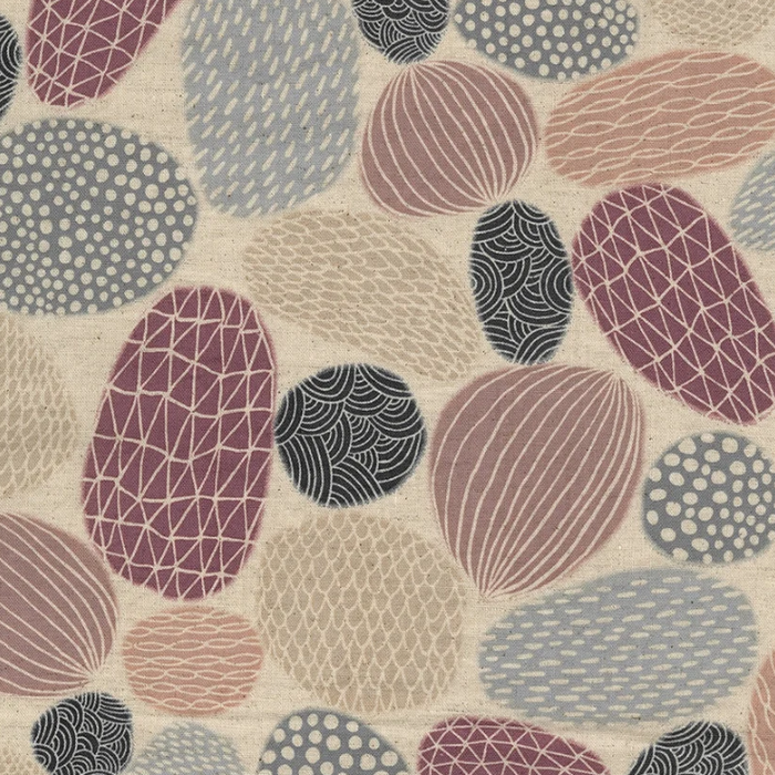A close-up of a patterned fabric featuring organic, pebble-like shapes in dusty pink, mauve, slate blue, charcoal, and cream on a textured off-white background.