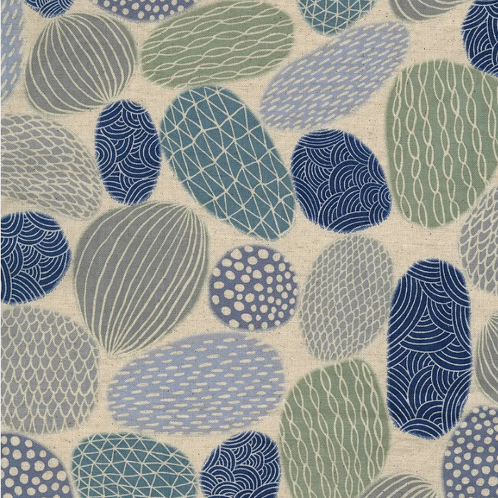 A close-up of a fabric or wallpaper pattern featuring organic, pebble-like shapes in muted blue, sage green, and gray on a warm off-white textured background.
