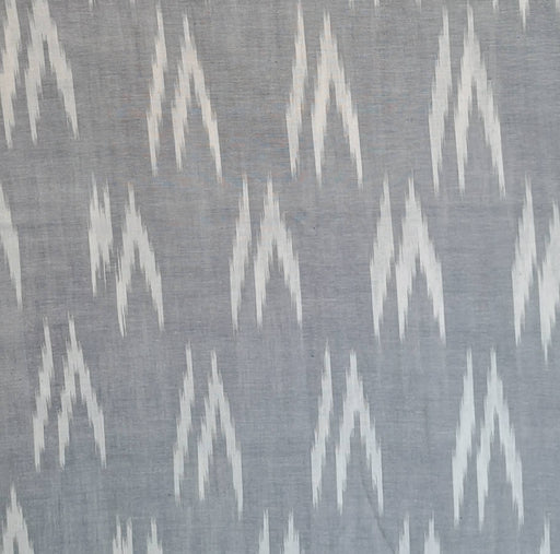 A close-up of a woven fabric with a repeating white ikat chevron pattern on a muted gray background.