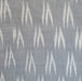 A close-up of a woven fabric with a repeating white ikat chevron pattern on a muted gray background.